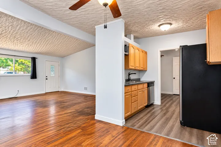 Kitchen featuring natural wood cabinetry, wood-finish flooring, and a sleek faucet, complemented by an open interior area with a ceiling fan and textured ceiling