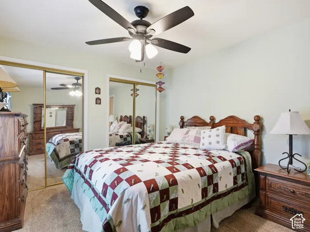 Room featuring neutral wall tones, wall-to-wall carpeting, dual floor-to-ceiling mirrored closet doors, and a central ceiling fan with integrated lighting