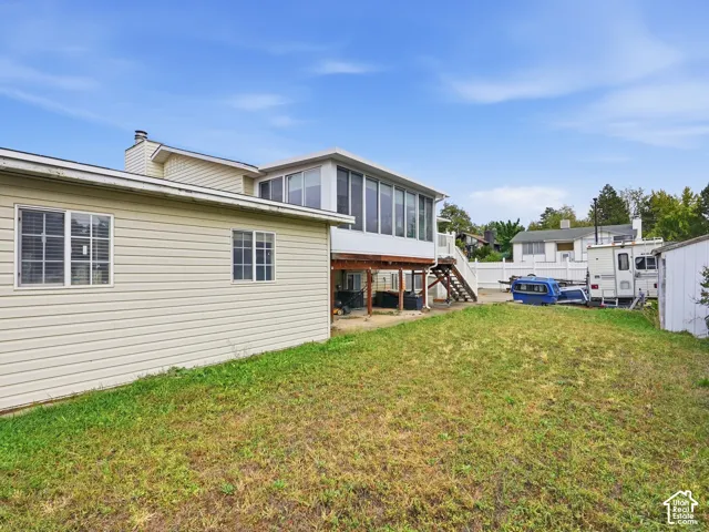 Rear exterior featuring vinyl siding, an elevated sunroom with expansive windows, a wooden deck with staircase, and a white privacy fence