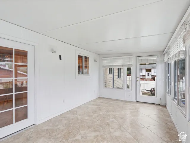Enclosed sunroom featuring vertical paneled walls, tile flooring, and multiple exterior access doors with glass inserts
