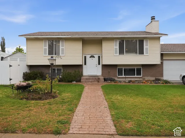 Split-level exterior featuring horizontal siding, brick masonry, a paved walkway, shingled roof, and an attached garage