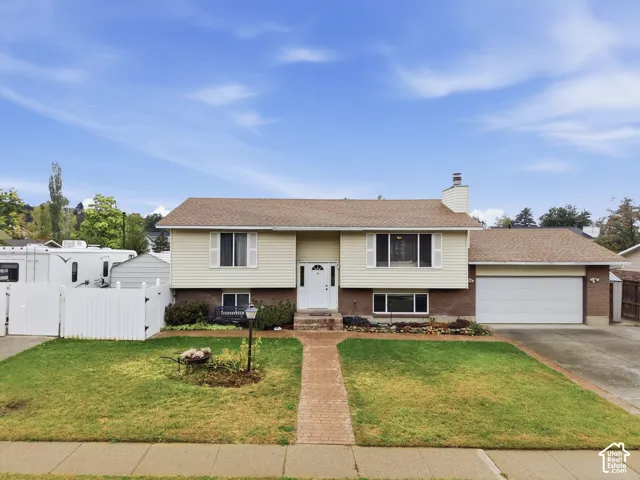 Split-level exterior featuring brick and vinyl siding, an attached two-car garage, white vinyl privacy fencing, and a brick paver walkway