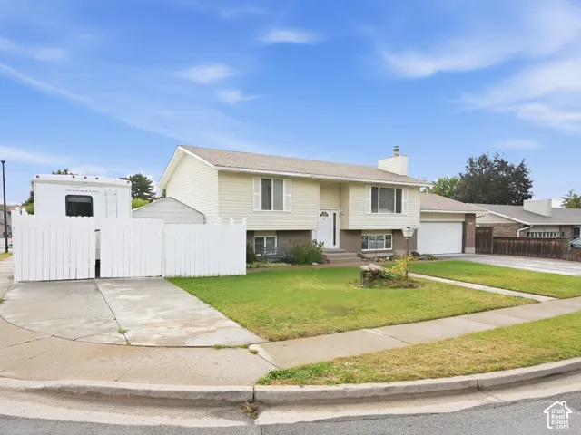 Split-level exterior featuring light-toned vinyl siding, brick accents, an attached two-car garage, and gated side-yard concrete parking
