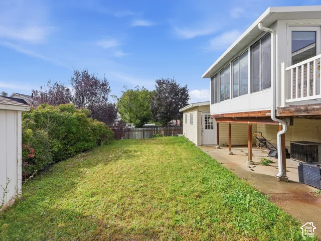 Fenced backyard featuring a concrete patio, an elevated enclosed sunroom, and mature perimeter landscaping