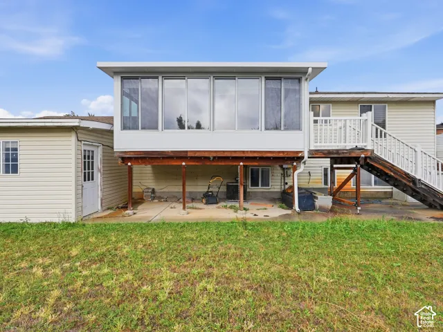 Rear exterior featuring an elevated enclosed sunroom, wood-framed deck with stairs, concrete patio, and horizontal siding