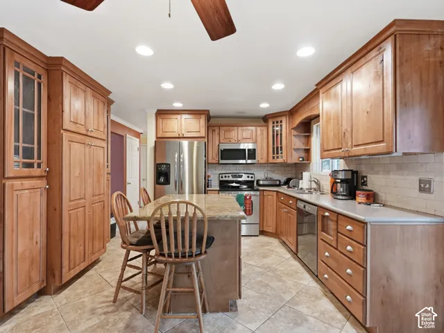 Kitchen featuring extensive wood cabinetry, stone-surfaced center island, stainless steel appliances, neutral tile flooring, and recessed ceiling lighting