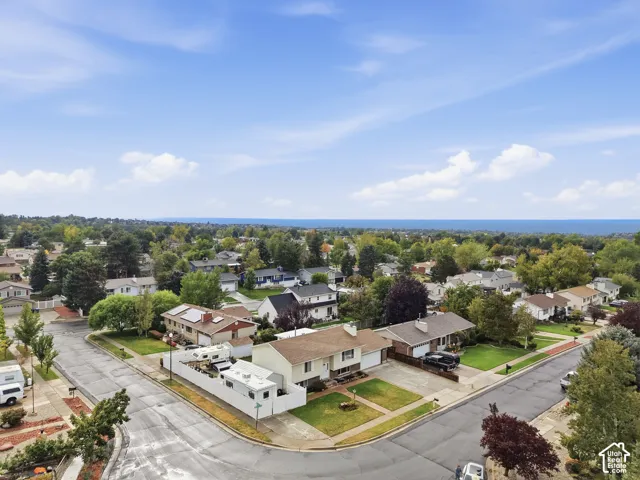 Aerial view showcasing a residential corner lot featuring a multi-level structure with an attached garage, prominent roof-mounted solar panels, and manicured front lawn