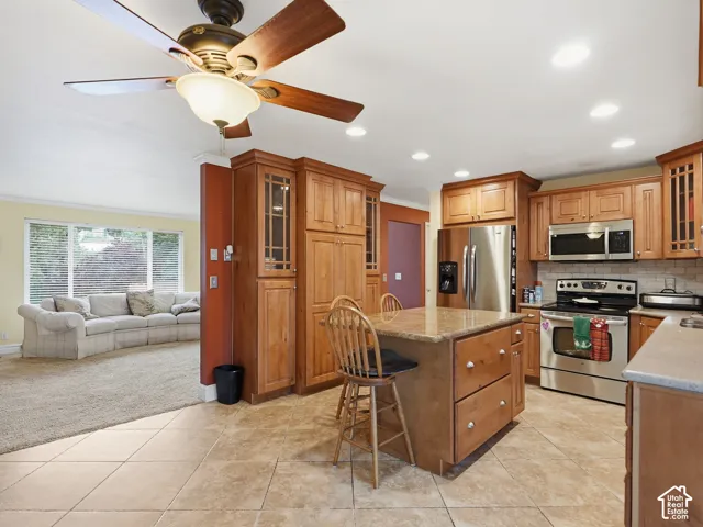 Kitchen featuring wood cabinetry, stone-topped center island, stainless steel appliances, tile flooring, and recessed lighting