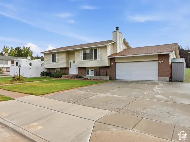 Split-level exterior featuring light horizontal siding, brick masonry detailing, a two-car garage, and a chimney