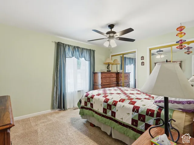 Bedroom featuring carpeting, dual mirrored closet doors, and a ceiling fan with integrated lighting