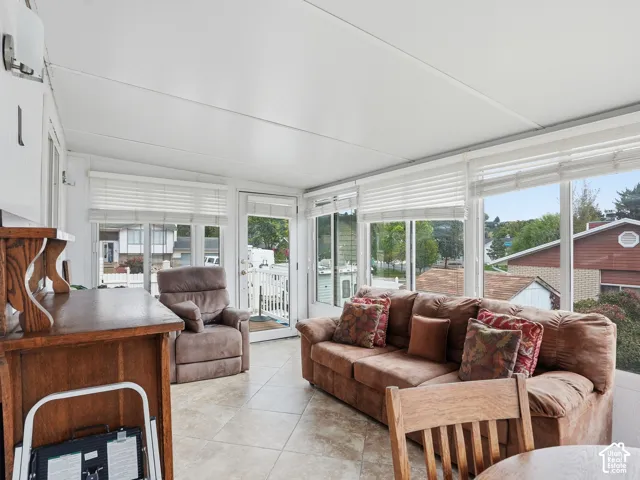 Enclosed sunroom featuring expansive windows with horizontal blinds, neutral tile flooring, and an exterior glass-panel door