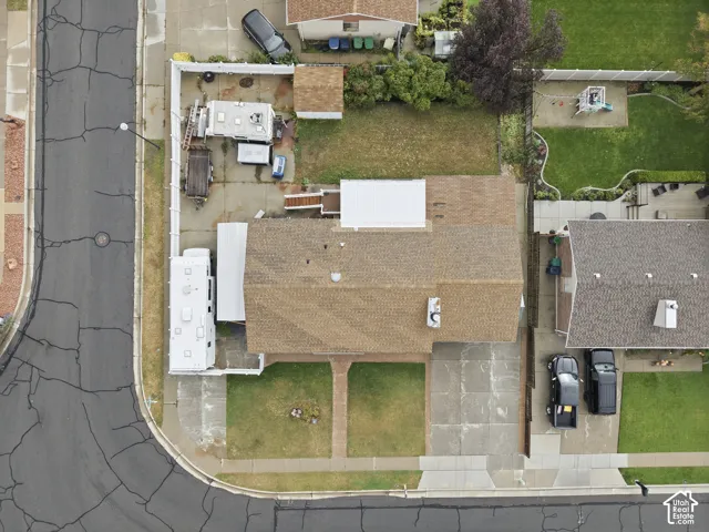 Aerial perspective of a corner lot property featuring a concrete driveway, gated side yard area, and a brick walkway