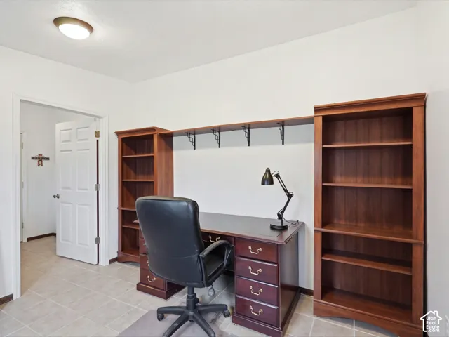 Built-in wood-finish shelving unit with integrated desk workspace and overhead storage, finished with tile flooring and a flush-mount ceiling light fixture