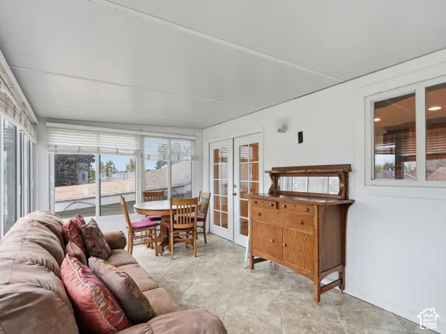 Sunroom featuring ceramic tile flooring, neutral wall paneling, numerous windows, and French doors