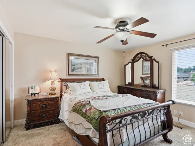 Room featuring neutral wall paint, carpeted flooring, a ceiling fan with integrated lighting, a sliding closet door, and a horizontal window with adjustable blinds