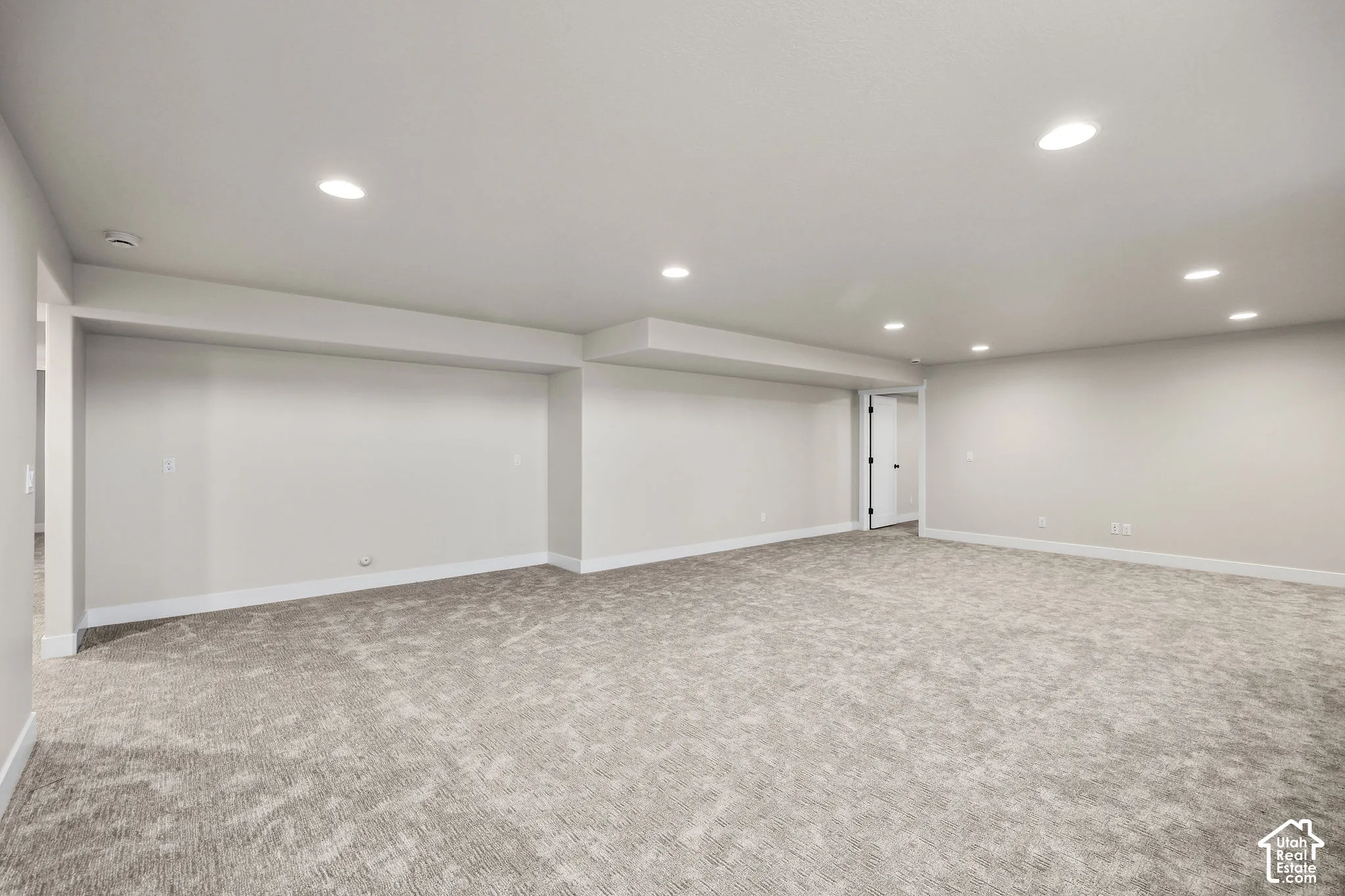 Expansive carpeted room featuring recessed lighting, light-toned walls, white baseboards, and a doorway with a dark-finished door