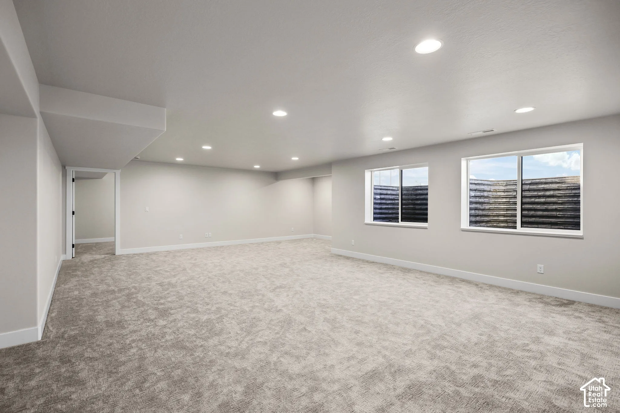 Spacious room featuring light gray carpeting, recessed ceiling lighting, and two egress windows