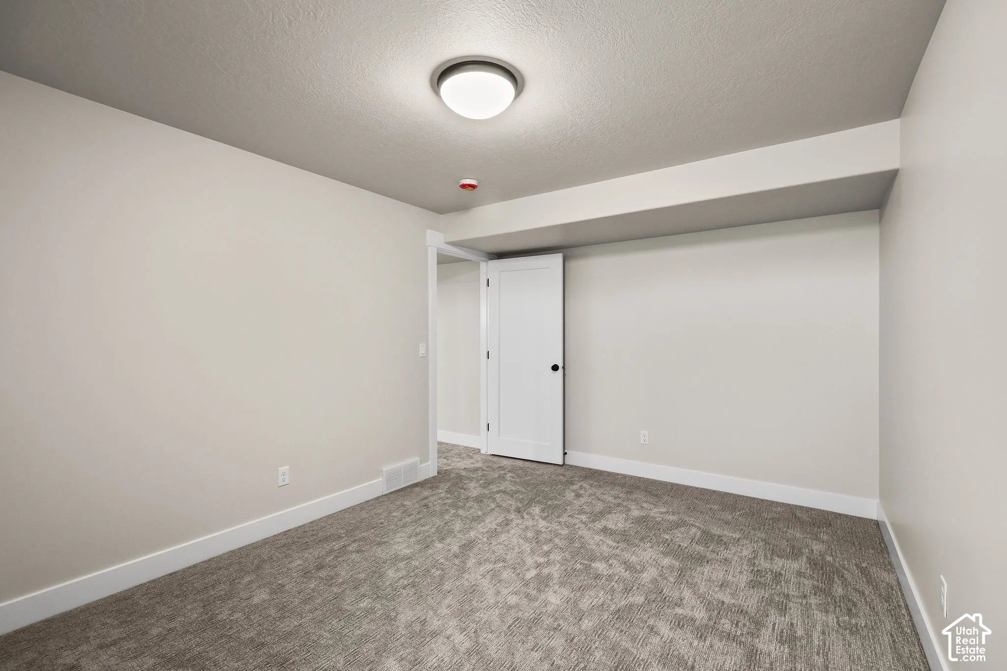 Carpeted room featuring a white interior door, recessed ceiling element, flush mount ceiling light, and baseboard trim
