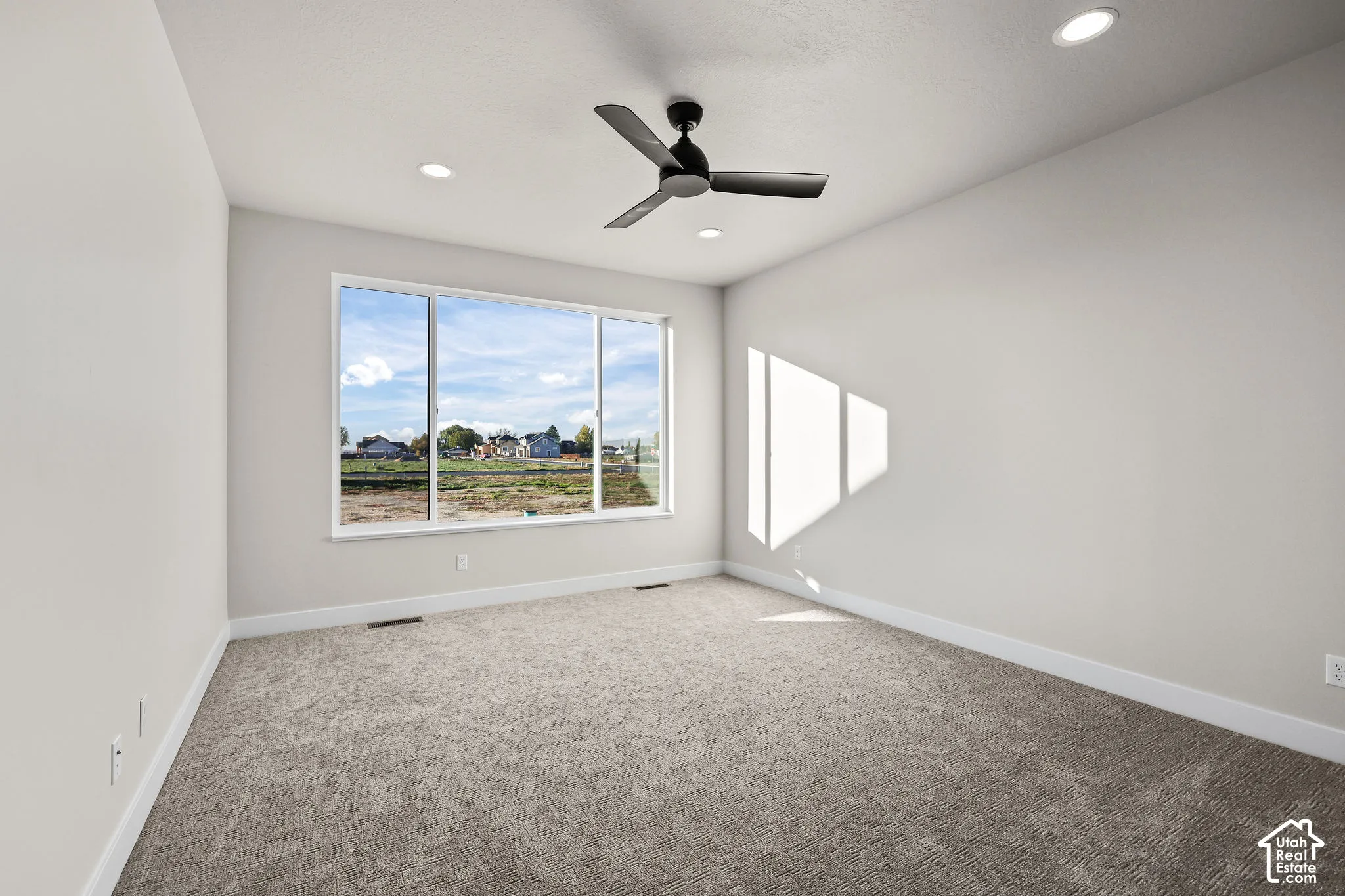 Room with a large multi-pane window, flush-mount ceiling fan, recessed lighting, and grey carpet flooring