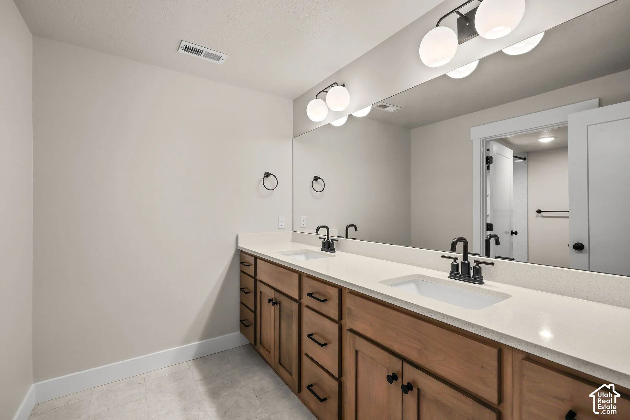 Dual vanity featuring wood-finish cabinetry, white countertops, and matte black fixtures