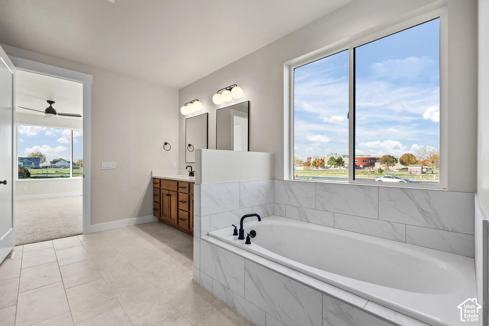 Tiled bathroom featuring a soaking tub with black fixtures, dual window, wood-finish vanity with dual sinks, and tile flooring