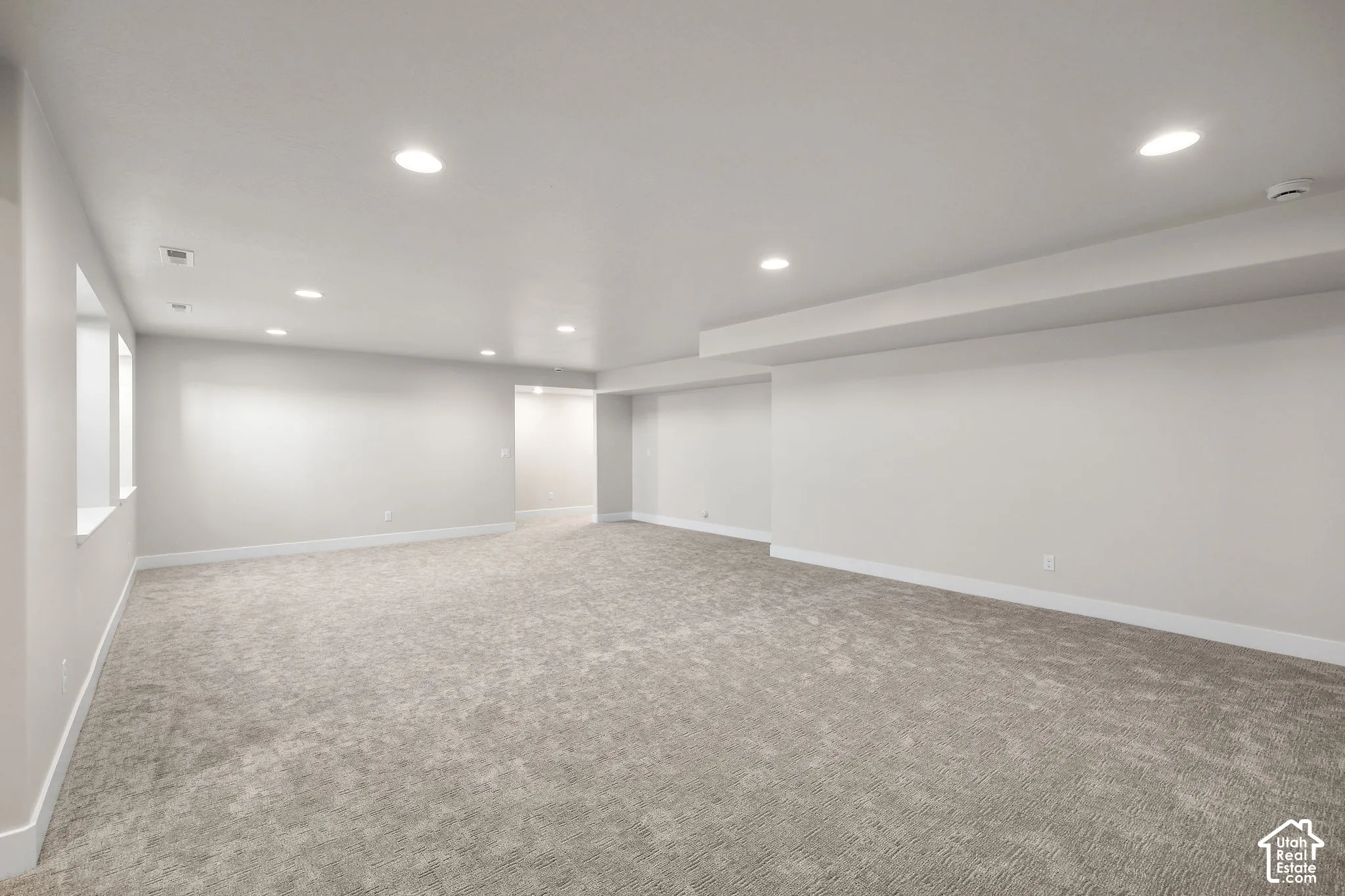 Expansive room featuring light gray carpeting, recessed ceiling lighting, and multiple windows