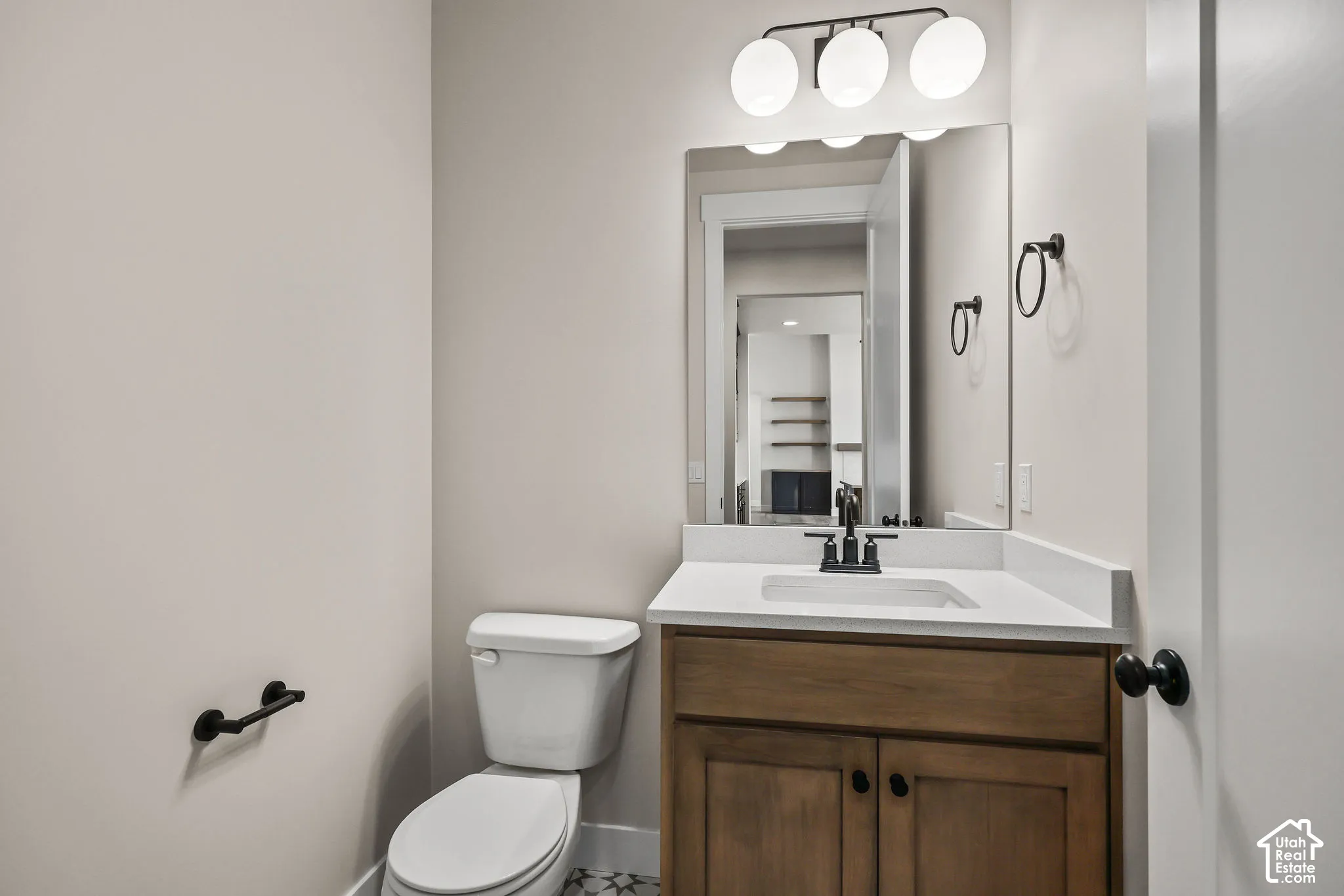 Bathroom featuring a wood-finish vanity with a white countertop and integrated sink, matte black faucet, and a wall-mounted mirror with a three-light vanity fixture