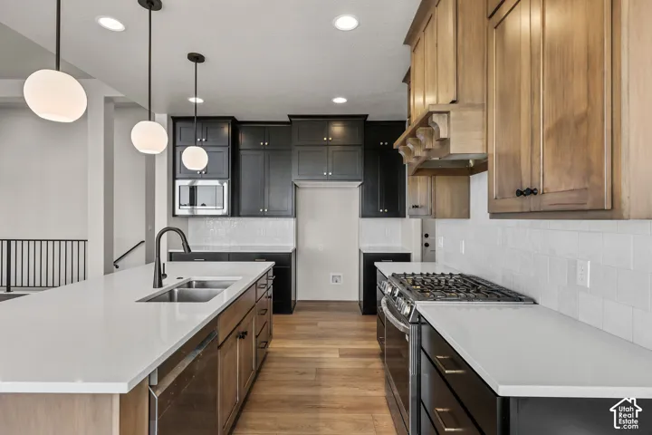 Contemporary kitchen featuring a large island with an undermount double sink and matte black faucet, light wood-finish flooring, white subway tile backsplash, stainless steel microwave, and a gas range
