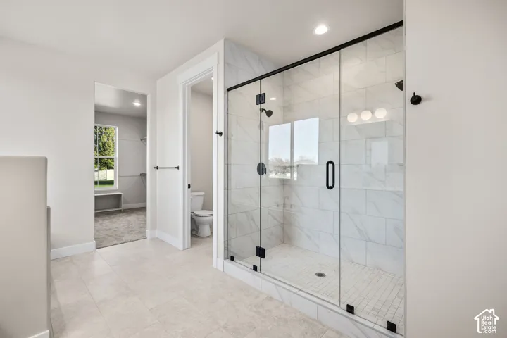 Spacious bathroom featuring a glass-enclosed shower with black fixtures, large format wall tiling, and a tiled shower pan