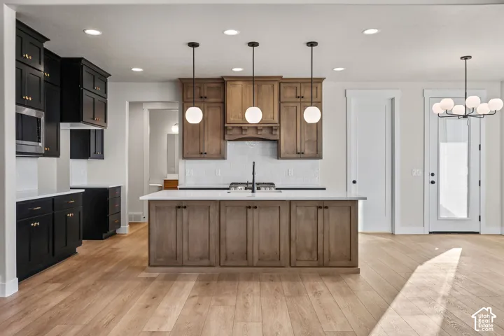 Spacious kitchen featuring a central island with integrated cooktop, wood-finish flooring, two-tone cabinetry, stainless steel appliances, and pendant lighting