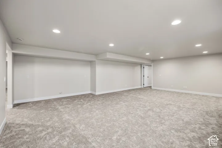 Expansive carpeted room featuring recessed lighting, light-toned walls, white baseboards, and a doorway with a dark-finished door