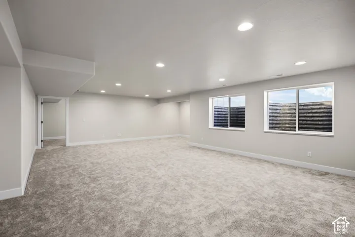 Spacious room featuring light gray carpeting, recessed ceiling lighting, and two egress windows