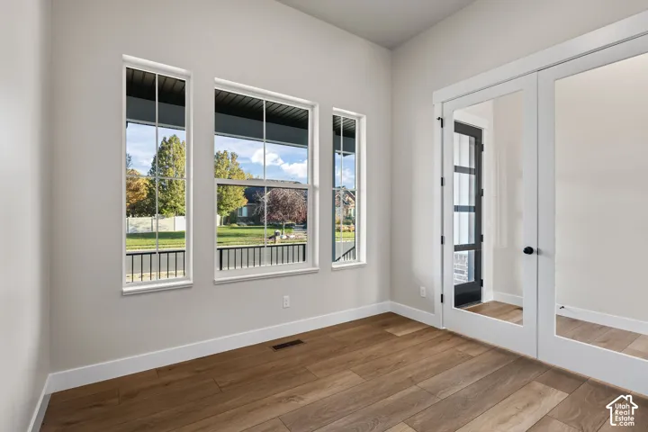 Room featuring expansive windows with white trim, wood-finish flooring, and a pair of glass French doors with matte black hardware