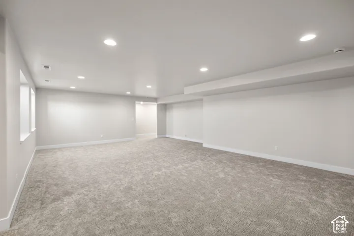 Expansive room featuring light gray carpeting, recessed ceiling lighting, and multiple windows