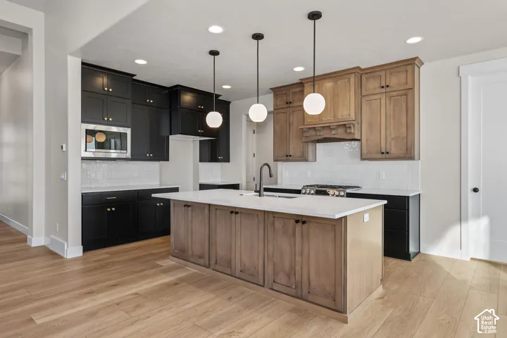 Open-concept kitchen featuring a large central island with a solid surface countertop, two-tone cabinetry, stainless steel appliances, a tile backsplash, and light wood-finish flooring
