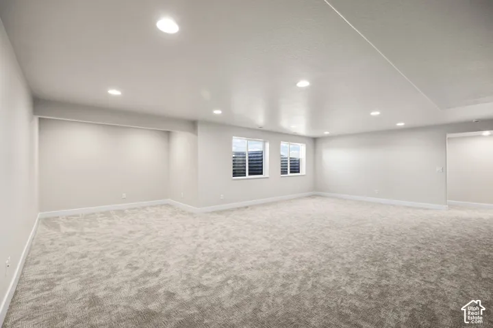 Spacious room featuring light gray carpeting, recessed ceiling lighting, two windows with horizontal blinds, and clean white baseboards
