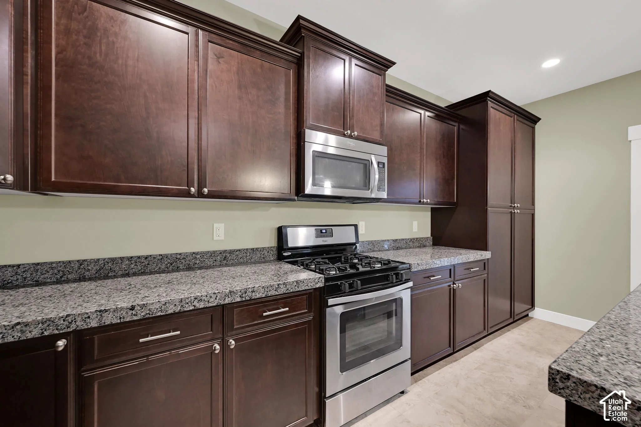 Dark wood cabinetry, stone countertops, stainless steel gas range, built-in microwave, and tile flooring