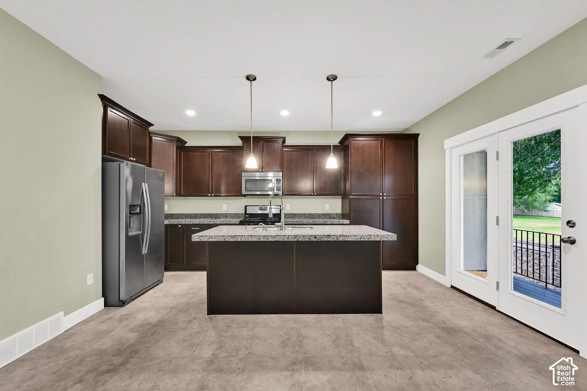 Kitchen featuring dark wood cabinetry, center island with stone-finish countertop, stainless steel appliances, and dual pendant lighting