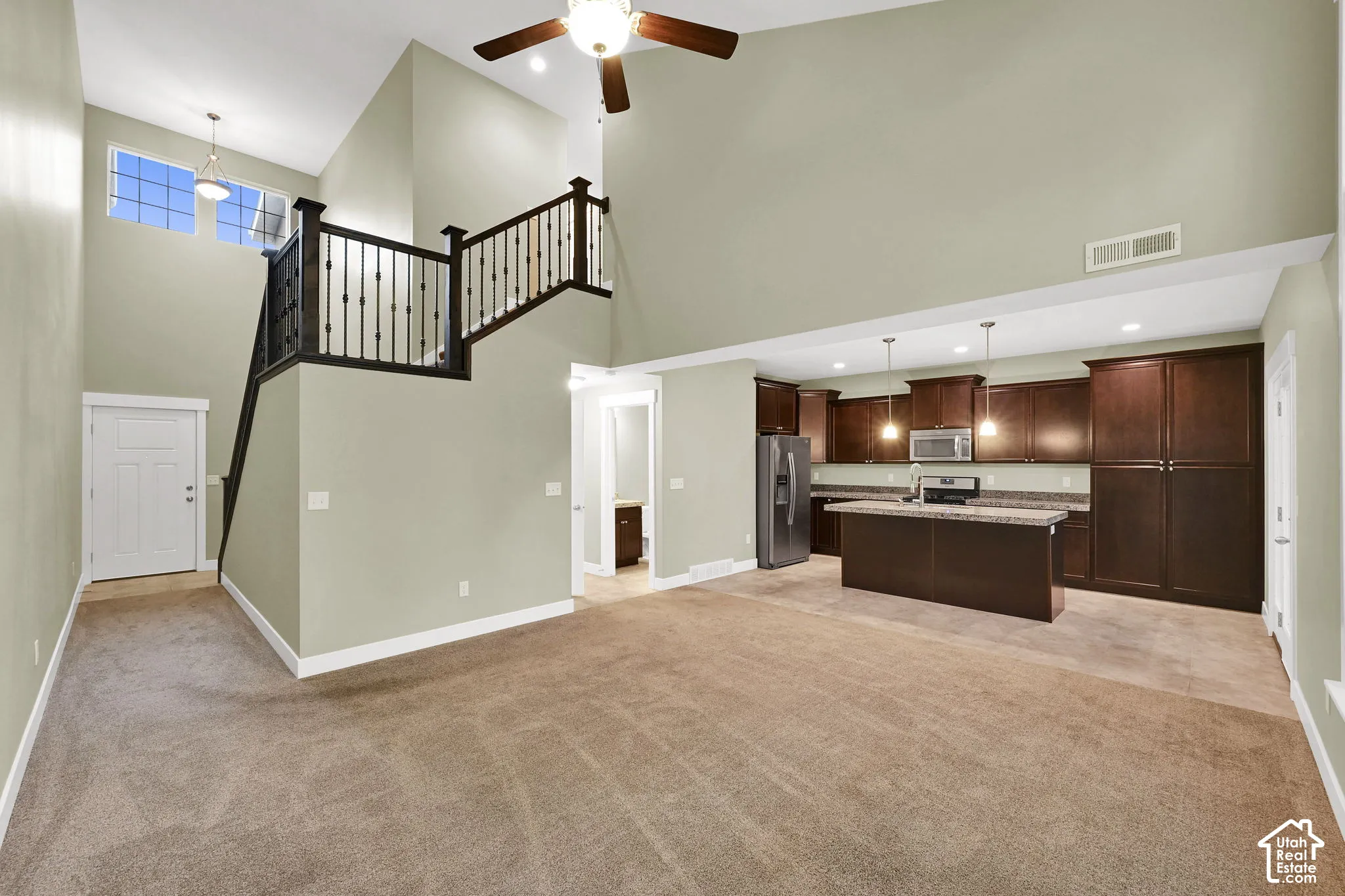 Vaulted ceilings, kitchen island with stone-surface countertop, dark wood cabinetry, and an open staircase with a metal railing