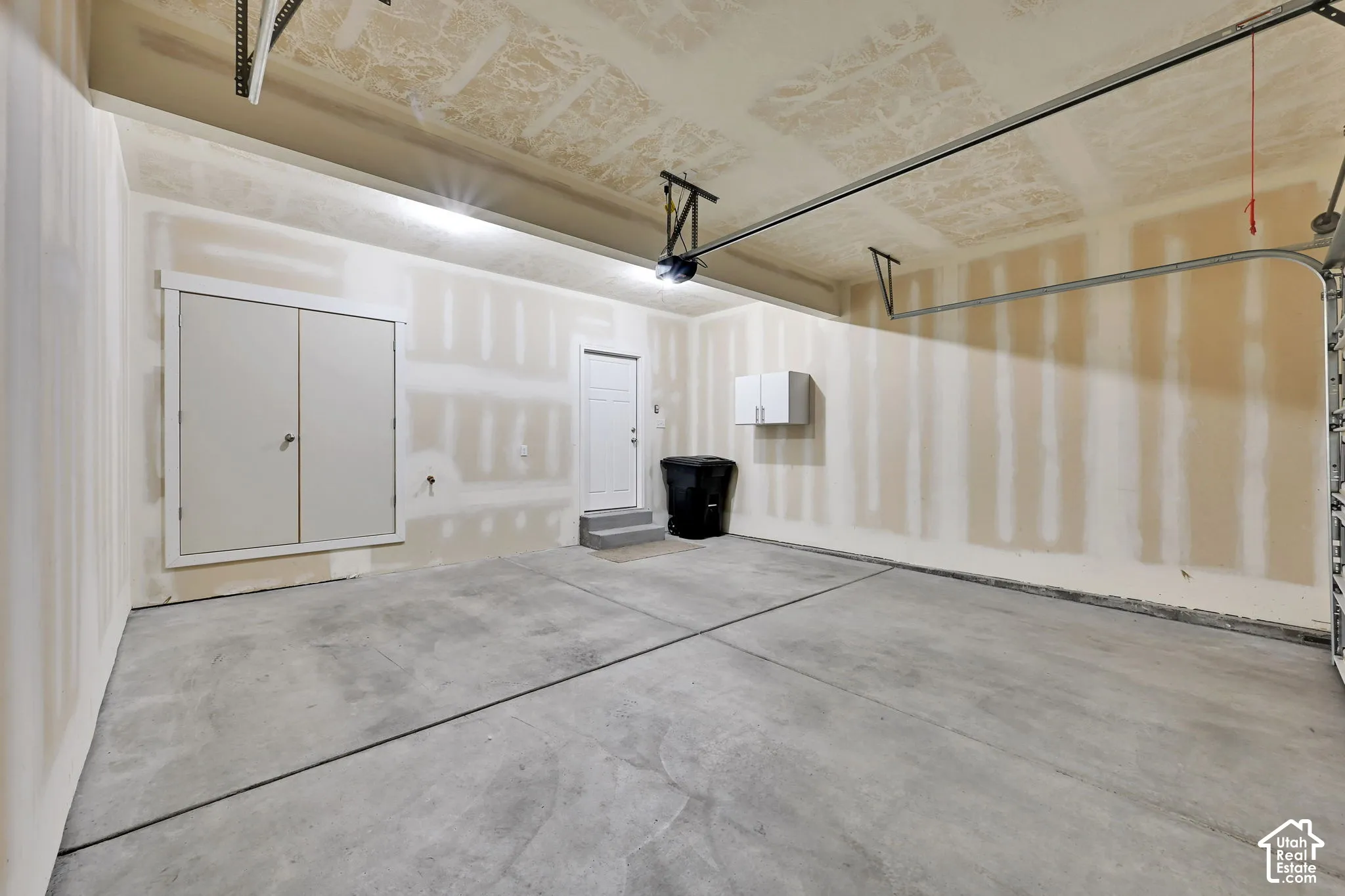 Spacious garage featuring concrete flooring, unpainted drywall, a built-in storage cabinet, and a pedestrian door