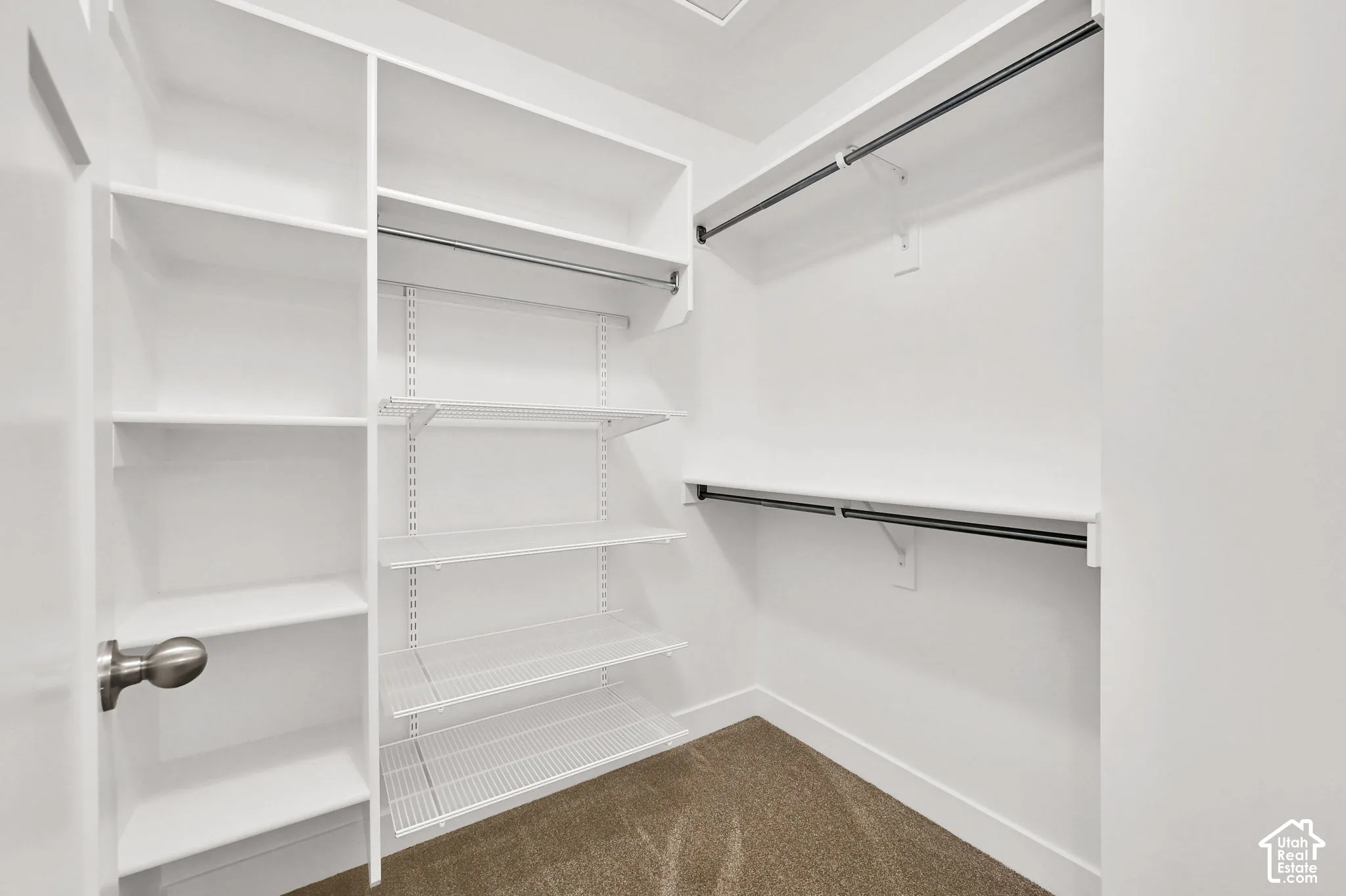 Walk-in closet featuring white built-in shelving, adjustable wire rack system, multi-level hanging rods, and neutral carpeting