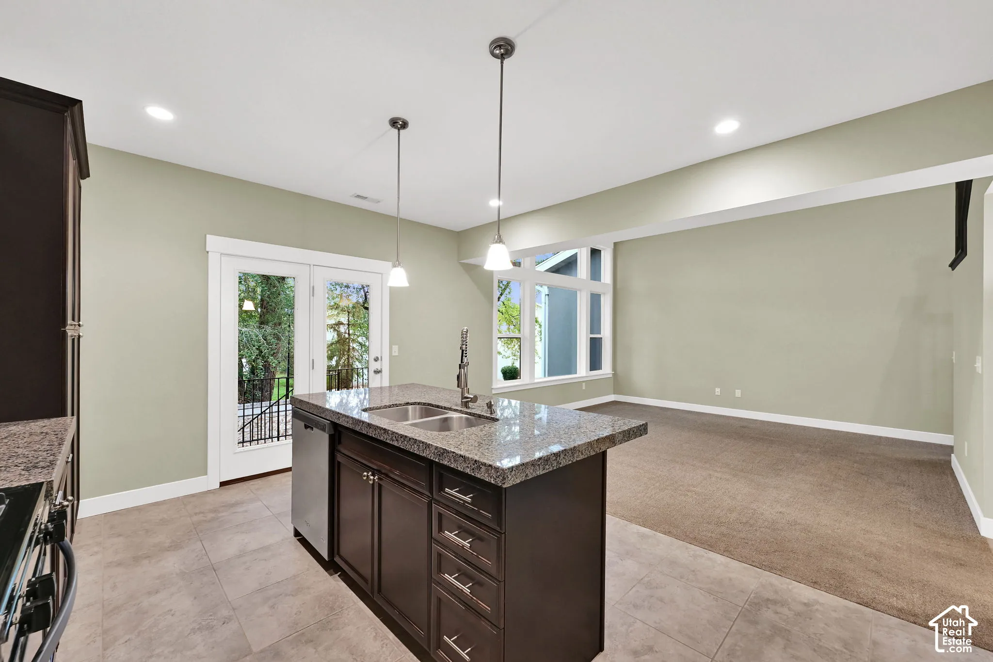 Kitchen island featuring stone countertops, dark-finish cabinetry, stainless steel dishwasher, dual-basin undermount sink, and dual pendant lighting