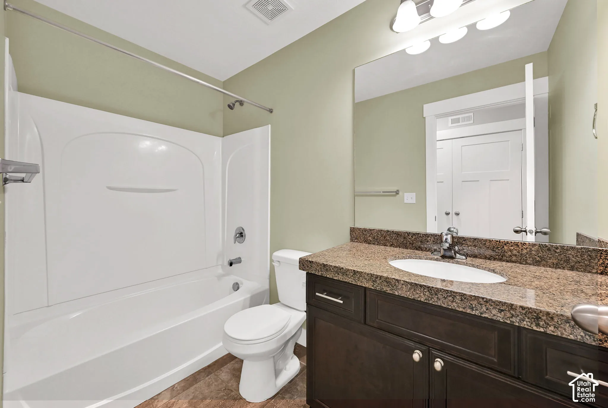Full bathroom featuring a white tub-and-shower combination, dark wood-finish cabinetry, a stone-composite countertop with an integrated oval sink, and a large wall-mounted mirror