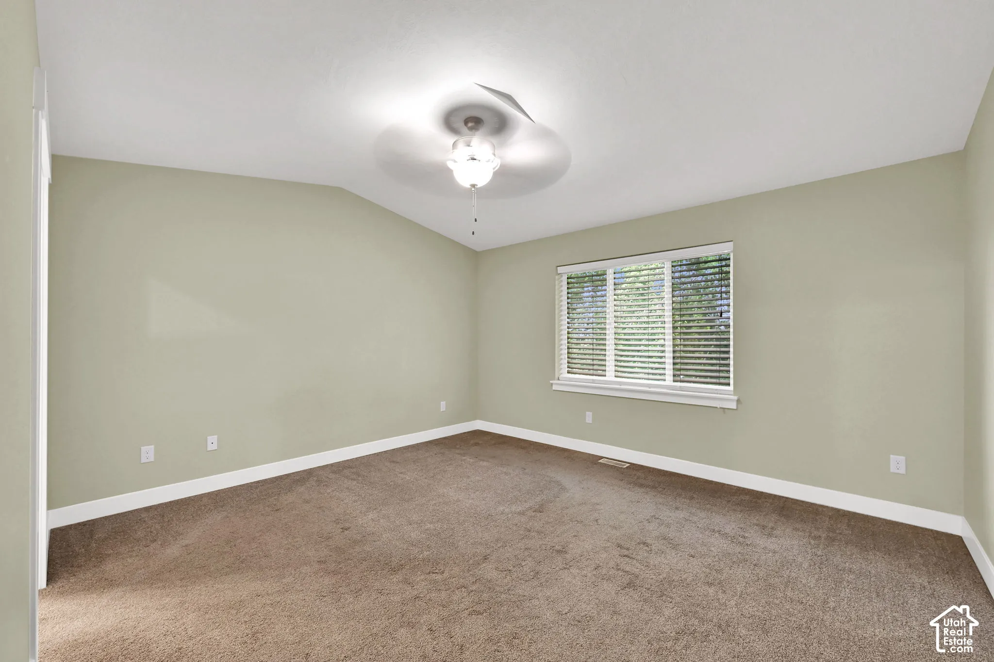 Room featuring a vaulted ceiling, neutral wall tones, wall-to-wall carpeting, a multi-blade ceiling fan with integrated lighting, and a window with horizontal blinds