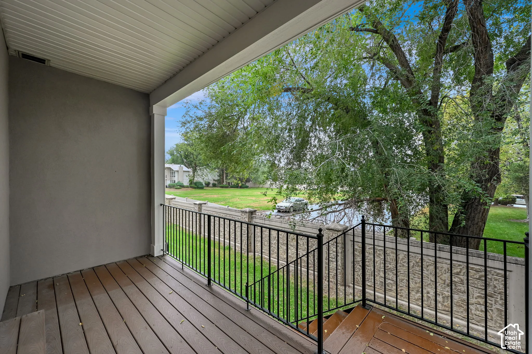 Covered porch featuring wood-finish decking, black metal railing, and staircase with access to a fenced outdoor area