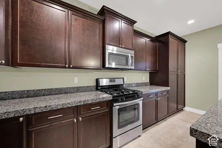 Dark wood cabinetry, stone countertops, stainless steel gas range, built-in microwave, and tile flooring