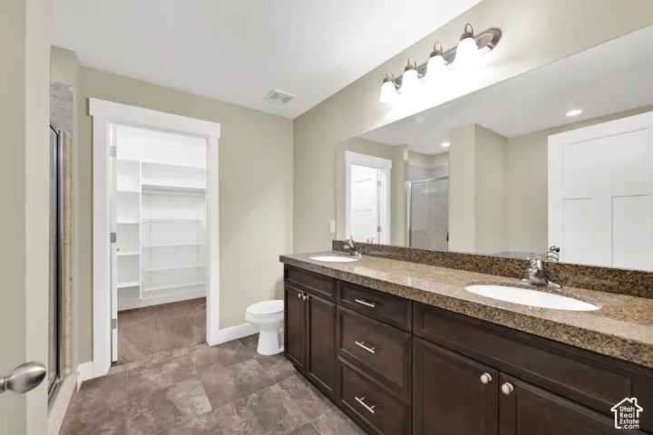 Double vanity featuring dark wood-finish cabinetry, stone-style countertop with dual undermount sinks, full-width mirror, and walk-in closet with built-in shelving