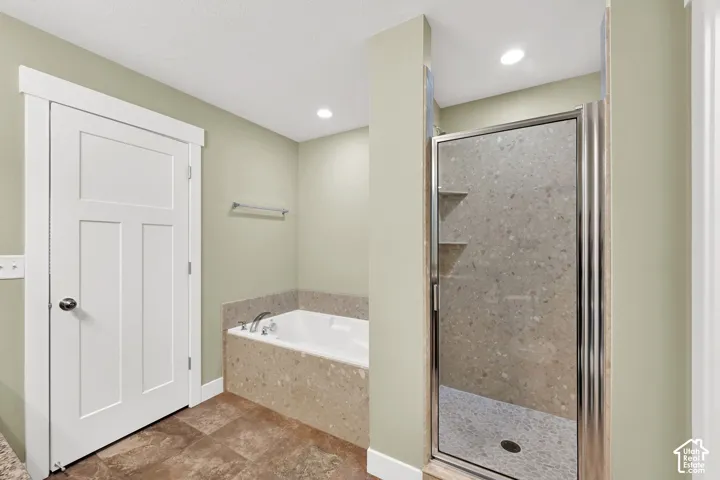 Soaking tub with stone-composite surround, walk-in shower with glass enclosure, integrated tile shelving, and tile flooring