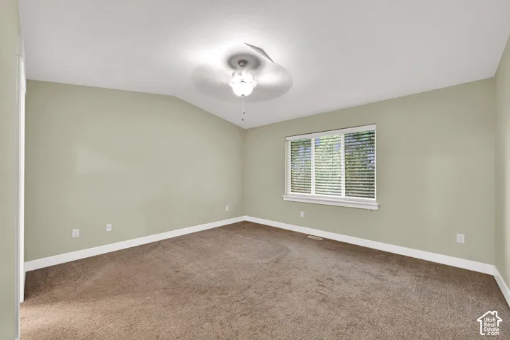 Room featuring a vaulted ceiling, neutral wall tones, wall-to-wall carpeting, a multi-blade ceiling fan with integrated lighting, and a window with horizontal blinds