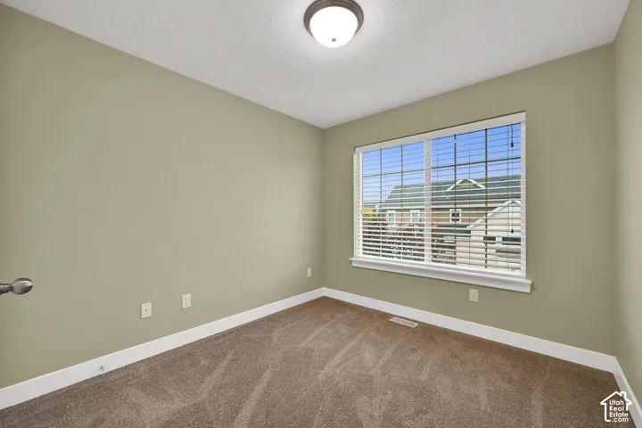 Room featuring neutral-toned carpeting, a large window with fitted horizontal blinds, and a circular flush-mount ceiling light fixture